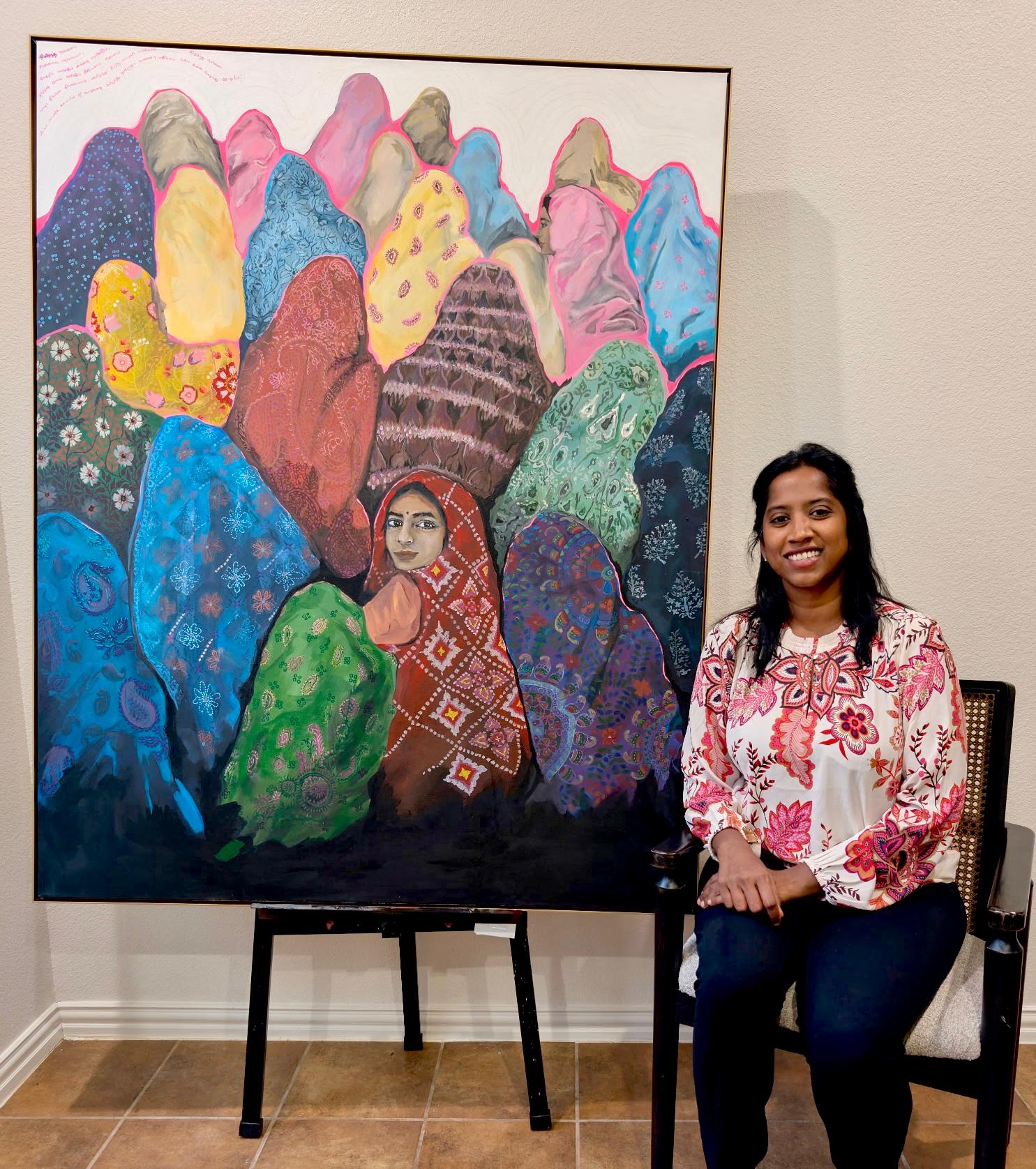Painting of women in colorful patterned head coverings, with Bharathi standing beside the canvas