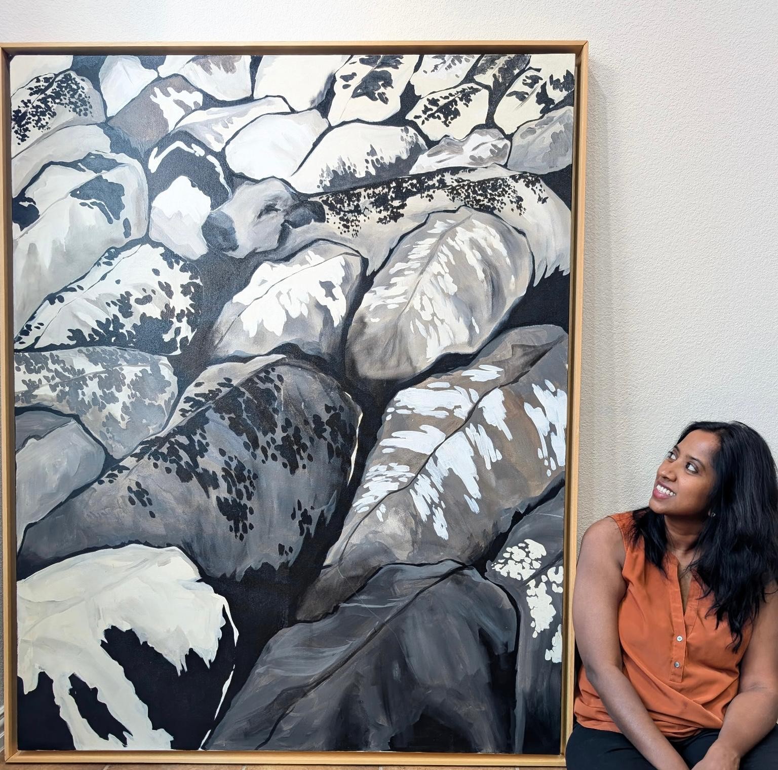 Black and white painting of longhorn cattle hide patterns from the Imperfections series, with Bharathi seated beside it